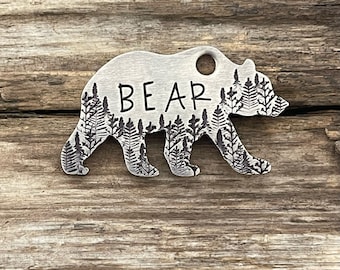 May include: A silver bear silhouette keychain with a forest design and the word "BEAR" engraved on the body.