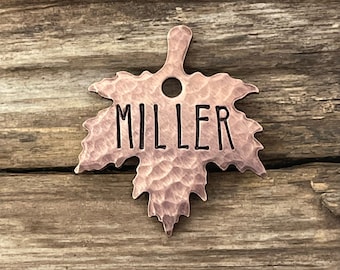 May include: A copper-colored maple leaf-shaped tag with a hole for a ring. The tag has the name "MILLER" engraved on it.