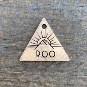 May include: A triangular brass tag with a mountain and sun design and the word "ROO" engraved on it.
