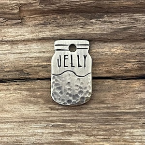 May include: Silver metal charm shaped like a jar with the word "JELLY" on the front. The jar has a hammered texture.