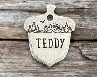 May include: A brass acorn-shaped pet tag featuring a mountain scene and the name "TEDDY" engraved on it.