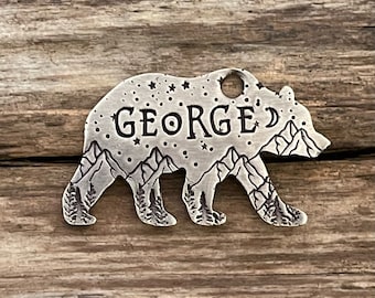 May include: Silver bear silhouette charm with a mountain and starry night scene engraved on the surface. The name "GEORGE" is engraved on the bear's back.