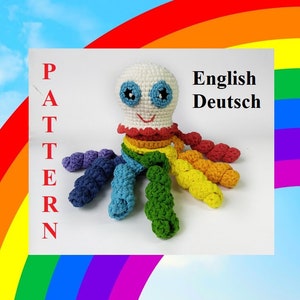 Può includere: Un giocattolo di polpo all'uncinetto arcobaleno con corpo bianco e occhi blu. Il giocattolo è su uno sfondo bianco con le parole "PATTERN" e "English Deutsch" in rosso.