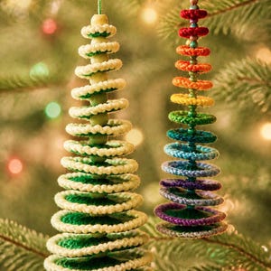 May include: Two cone-shaped Christmas tree ornaments hanging from a branch. The larger ornament features stacked cream and green crocheted rings with wooden beads. The smaller ornament displays a rainbow gradient of crocheted rings.