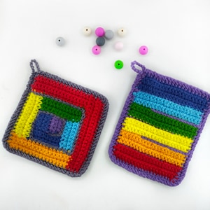May include: Two colorful crocheted pot holders, one with a rainbow square pattern and the other with horizontal rainbow stripes. Both pot holders have a purple border.