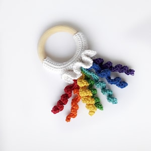 May include: A crocheted rainbow teether with a wooden ring. The rainbow is made of colorful yarn and is attached to the ring with a white crocheted cloud.