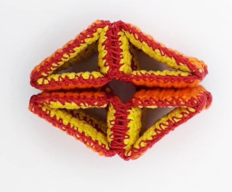 May include: A crocheted geometric starburst in shades of red, orange, and yellow.