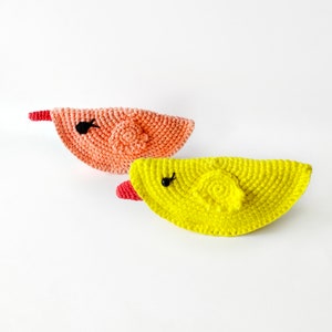 May include: Two crocheted bird ornaments, one in a peach colour and one in a bright yellow colour. Both birds have black eyes and red beaks.