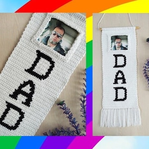 May include: White crocheted wall hanging with the word "DAD" spelled out in black yarn. A photo is inserted into a frame at the top of the hanging.