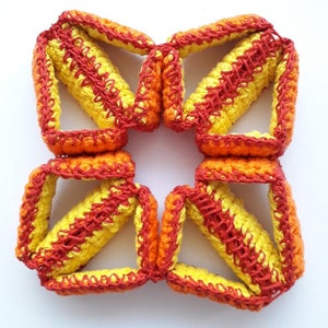 May include: A crocheted flower-shaped object made of yellow and orange yarn. The flower is made of multiple connected pieces, each with a diamond shape.