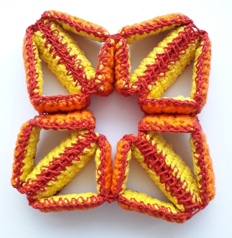 May include: A crocheted flower-shaped object made of yellow and orange yarn. The flower is made of multiple connected pieces, each with a diamond shape.