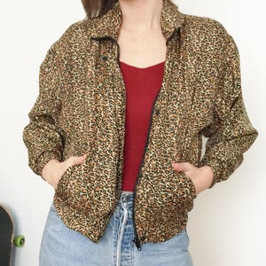 Puede incluir: Una chaqueta de color marrón y negro con estampado de leopardo y cierre de cremallera. La chaqueta tiene un cuello alto y dos bolsillos.