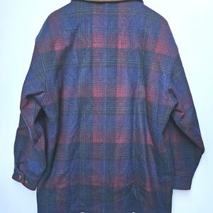 May include: A vintage plaid jacket in shades of blue, red, and black, with a brown collar. The jacket is hanging on a wooden hanger. The back of the jacket is visible, showcasing the plaid pattern and buttoned cuffs.