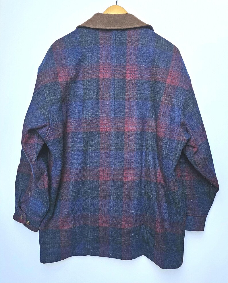 May include: A vintage plaid jacket in shades of blue, red, and black, with a brown collar. The jacket is hanging on a wooden hanger. The back of the jacket is visible, showcasing the plaid pattern and buttoned cuffs.