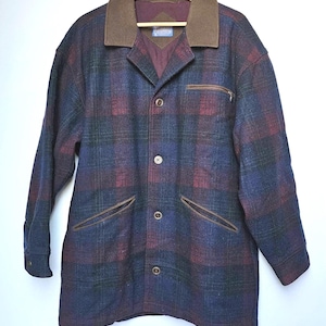 May include: A plaid wool jacket in shades of blue, burgundy, and green, featuring a brown collar and pocket trim. The jacket has a button-up front, a zippered chest pocket, and two front pockets. It is hanging on a wooden hanger.