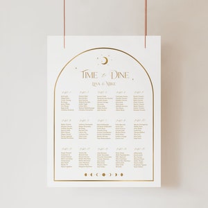 May include: A white wedding seating chart with gold lettering and design elements. The text reads "Time & Dine" above the names of guests, organized by table number. The design includes a crescent moon and stars.