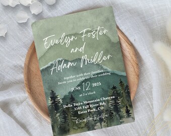 Op de afbeelding: Een trouwuitnodiging met een aquarel berglandschap in groen- en grijstinten. De namen "Evelyn Foster en Adam Miller" staan in een elegant lettertype. De uitnodiging bevat de datum, tijd en locatie: Della Terra Mountain Chateau, Estes Park, CO.