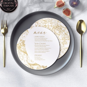 May include: A formal place setting with a gray plate, gold utensils, and a menu. The menu features a gold map design and the word "menu" in elegant script. Fresh figs are placed on the white cloth.