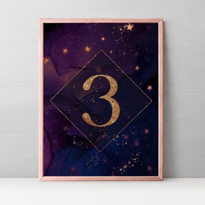 May include: Framed art print featuring a dark blue and purple abstract background with gold stars and accents. A gold diamond shape contains the number 3 in gold glitter. The frame is a rose gold color.
