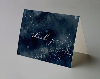 Puede incluir: Una tarjeta de agradecimiento plegada con un fondo de acuarela azul oscuro y texto blanco. La tarjeta presenta un diseño de constelación y las palabras "thank you" en escritura elegante.