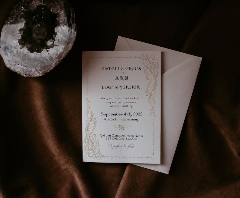 Może przedstawiać: Kremowe zaproszenie ślubne ze złotymi detalami i eleganckim pismem. Zaproszenie zawiera nazwiska Estelle Green i Logan Mercier, datę i godzinę ślubu. Obok znajduje się biała koperta.