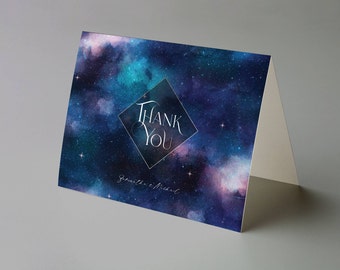 Puede incluir: Tarjeta de agradecimiento plegada con un diseño de acuarela de galaxia en tonos azules, morados y turquesas. Las palabras "Thank You" están en una fuente blanca dentro de un diamante. Los nombres "Jonathan & Michael" están escritos debajo.