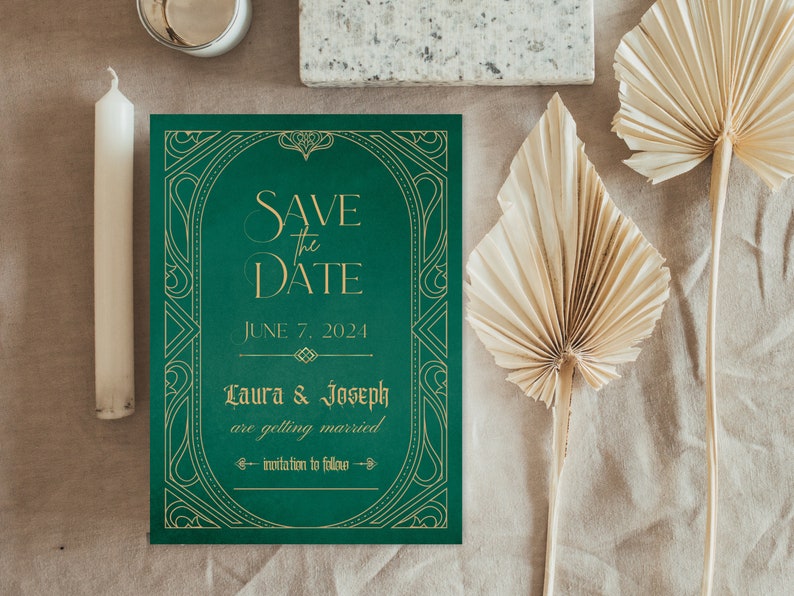 May include: Emerald green "Save the Date" card with gold Art Deco style lettering and design. The card reads "Save the Date" and "June 7, 2024" with the names "Laura & Joseph" and "invitation to follow". A white candle and dried palm leaves are also visible.