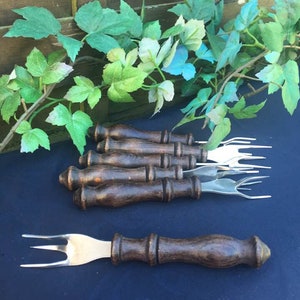 May include: Set of six wooden handled forks with silver tines. The forks are arranged in a fan shape on a blue surface.