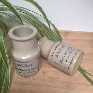 Puede incluir: Dos pequeños tarros de cerámica con etiquetas azules y blancas que dicen "Maille Mostaza de Dijon al vino blanco".