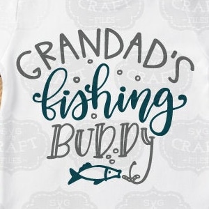 K&ouml;nnte beinhalten: Ein wei&szlig;es T-Shirt mit dem Text "Grandad's Fishing Buddy" in grauer und blaugr&uuml;ner Schrift. Unter dem Text befindet sich ein kleiner blaugr&uuml;ner Fisch mit einer Angelschnur.