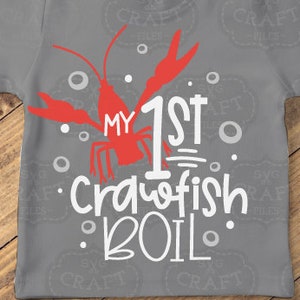Puede incluir: Una camiseta gris con un diseño de cangrejo rojo y el texto "My 1st Crawfish Boil".