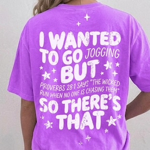 May include: A bright purple short-sleeve t-shirt featuring white distressed text on the back that reads: I WANTED TO GO JOGGING BUT PROVERBS 28:1 SAYS THE WICKED RUN WHEN NO ONE IS CHASING THEM SO THERE'S THAT, accented with small white star graphics.