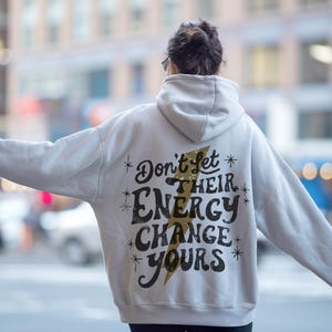 May include: A white hoodie with a black and gold graphic that says "Don't let their energy change yours".