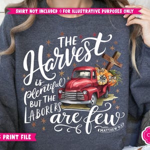 May include: A dark blue sweatshirt with a white graphic design featuring a red truck carrying pumpkins and a cross. The text reads "The Harvest is Plentiful But The Laborers Are Few" with the scripture reference "Matthew 9:37".
