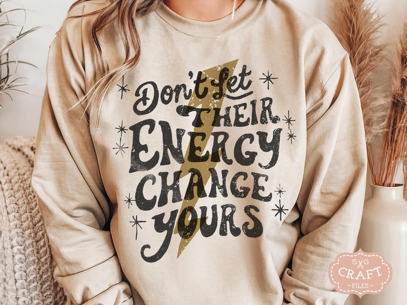 May include: A beige sweatshirt with a black graphic print that reads "Don't Let Their Energy Change Yours" with a gold lightning bolt design.