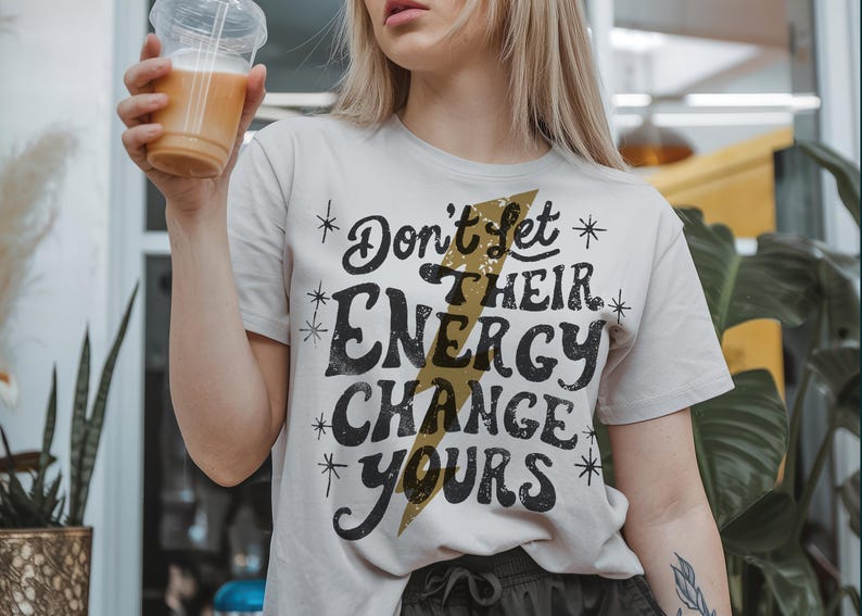 May include: White t-shirt with a black graphic that says "Don't Let Their Energy Change Yours" with a gold lightning bolt design.
