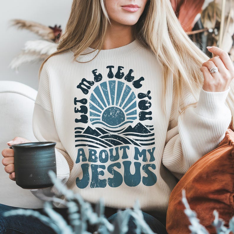 May include: A white sweatshirt with a blue and white graphic design. The graphic features a sun, waves, and the text "Let me tell you about my Jesus".