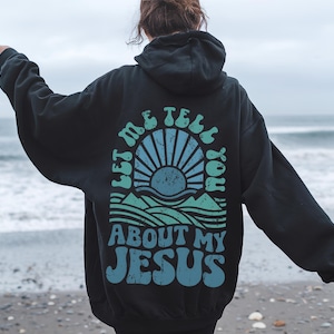 May include: Black hooded sweatshirt with a graphic print of a sunrise over a mountain range and the text "Let me tell you about my Jesus".