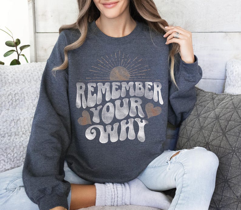 May include: A dark gray sweatshirt with a vintage-style graphic that says "Remember Your Why" in white with a sun and hearts.