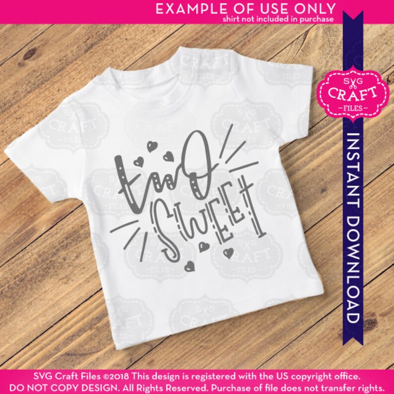 May include: A white t-shirt with the text "two sweet" in gray lettering with hearts and rays of light around the text. The shirt is on a wooden surface.