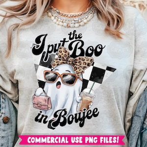 May include: A gray t-shirt with the text "I put the Boo in Boujee" in black and white lettering. A cartoon ghost wearing sunglasses and a leopard print headband is holding a pink purse and a cup of coffee. The background is a black and white checkered pattern.
