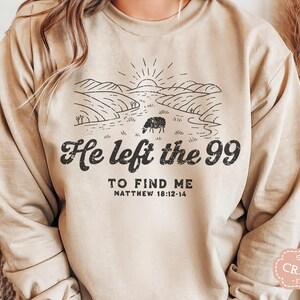 May include: A beige sweatshirt with a black graphic design of a sheep in a field with the text "He left the 99 to find me Matthew 18:12-14".