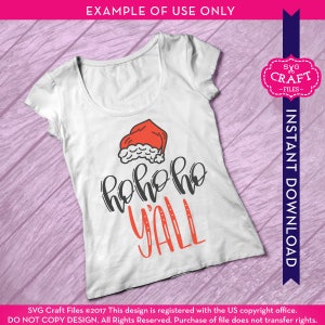 Puede incluir: Camiseta blanca con un gorro de Pap&aacute; Noel rojo y el texto "hoho ho y'all" en negro.