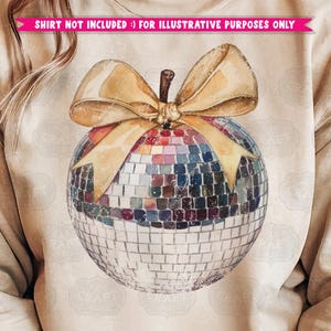 May include: A beige sweatshirt with a gold bow and a disco ball ornament. The ornament is a silver sphere with mirrored tiles.