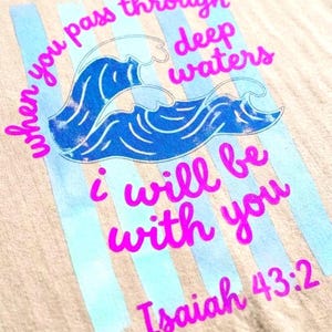 May include: A light beige t-shirt with a blue wave design and vertical light blue stripes. The shirt features the text "When you pass through deep waters, I will be with you, Isaiah 43:2" in bright pink.