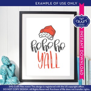 Puede incluir: Una impresi&oacute;n enmarcada blanca con un gorro de Pap&aacute; Noel rojo y blanco y el texto "hohoho yall" en letras negras y rojas.