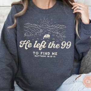 May include: A dark blue sweatshirt with a white graphic design of a sheep in a field. The text "He left the 99 to find me Matthew 18:12-14" is printed on the sweatshirt.