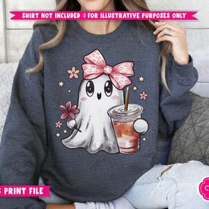 May include: A dark blue sweatshirt with a cute cartoon ghost wearing a pink bow and holding a cup of coffee. The ghost has a friendly face and is surrounded by small pink flowers.