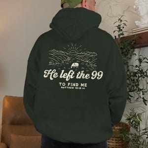 May include: A dark green hooded sweatshirt with a white graphic print of a sheep in a field with the text "He left the 99 to find me Matthew 18:12-14".