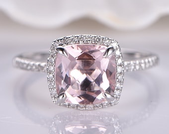 Könnte beinhalten: Ein quadratischer Ring mit einem rosafarbenen Edelstein und einem Heiligenschein aus kleineren Diamanten. Die Ringschiene ist ebenfalls mit kleineren Diamanten besetzt.